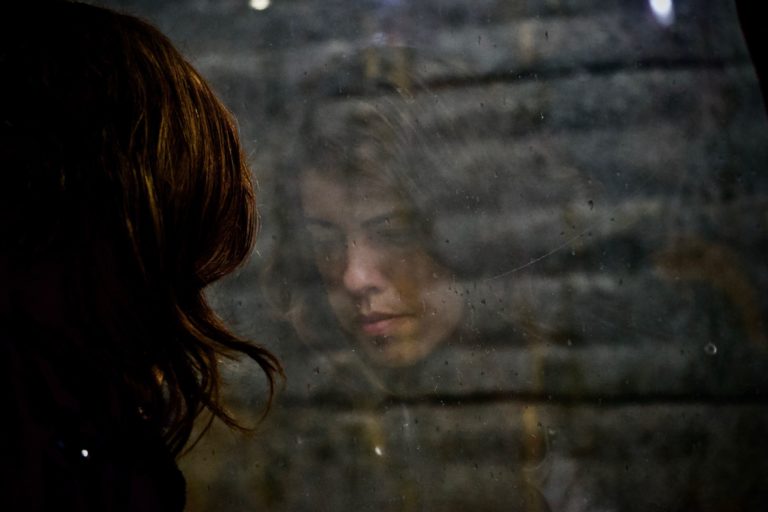 woman staring into window reflection. she has panic disorder