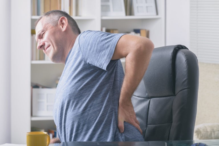 middle aged man sitting in computer chair clutching lower back due to bulging disc