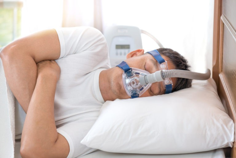 man with sleep apnea in bed with cpap machine in bright room