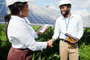 man and woman engineer shaking hands in front of solar panels