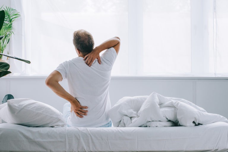 man in all white room stretching in the morning due to pain associated with Intervertebral Disc Syndrome IVDS