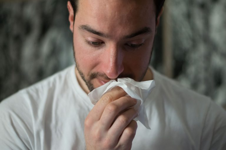 man in white shirt looking down and blowing his nose due to sinusitis
