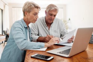 Older couple sitting at a table and researching Medicare on a laptop.